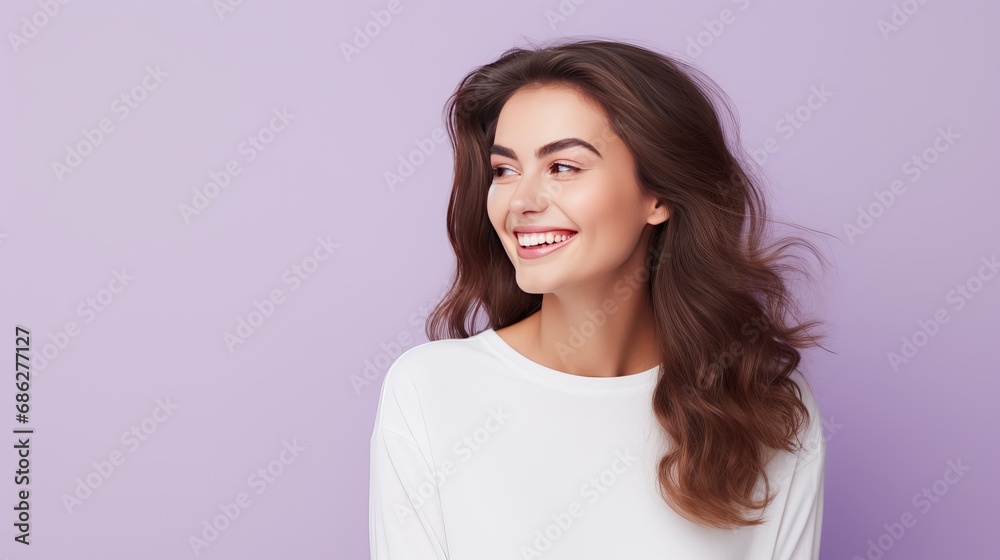 A photograph of an optimistic, lovely woman with straight hair holding her hands under her chin. She is wearing a white jumper and posing happily against a purple wall, demonstrating the A photograph of an optimistic, lovely woman with straight hair holding her hands under her chin. She is wearing a white jumper and posing happily against a purple wall, demonstrating the