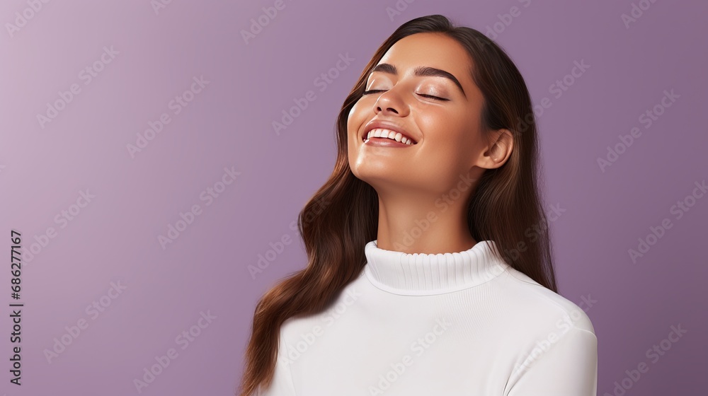 A photograph of an optimistic, lovely woman with straight hair holding her hands under her chin. She is wearing a white jumper and posing happily against a purple wall, demonstrating the A photograph of an optimistic, lovely woman with straight hair holding her hands under her chin. She is wearing a white jumper and posing happily against a purple wall, demonstrating the