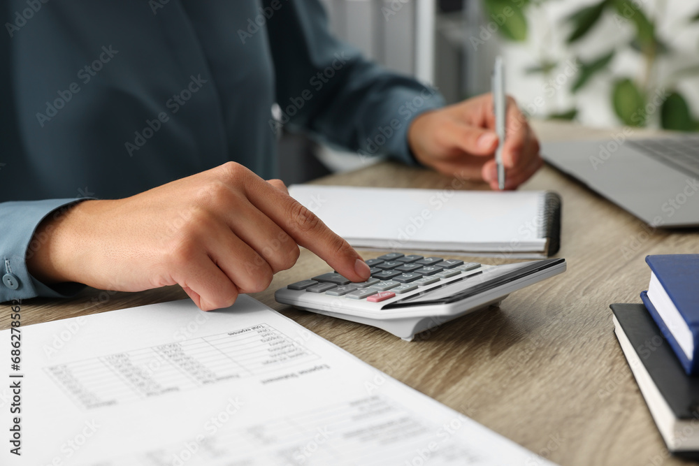Woman using calculator while taking notes at wooden table, closeup Woman using calculator while taking notes at wooden table, closeup