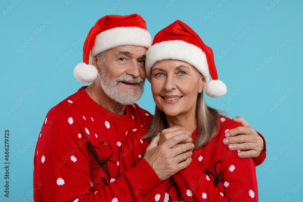 Senior couple in Christmas sweaters and Santa hats on light blue background Senior couple in Christmas sweaters and Santa hats on light blue background