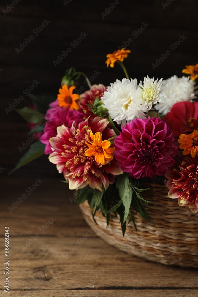 Beautiful wild flowers and leaves in wicker basket on wooden table, closeup