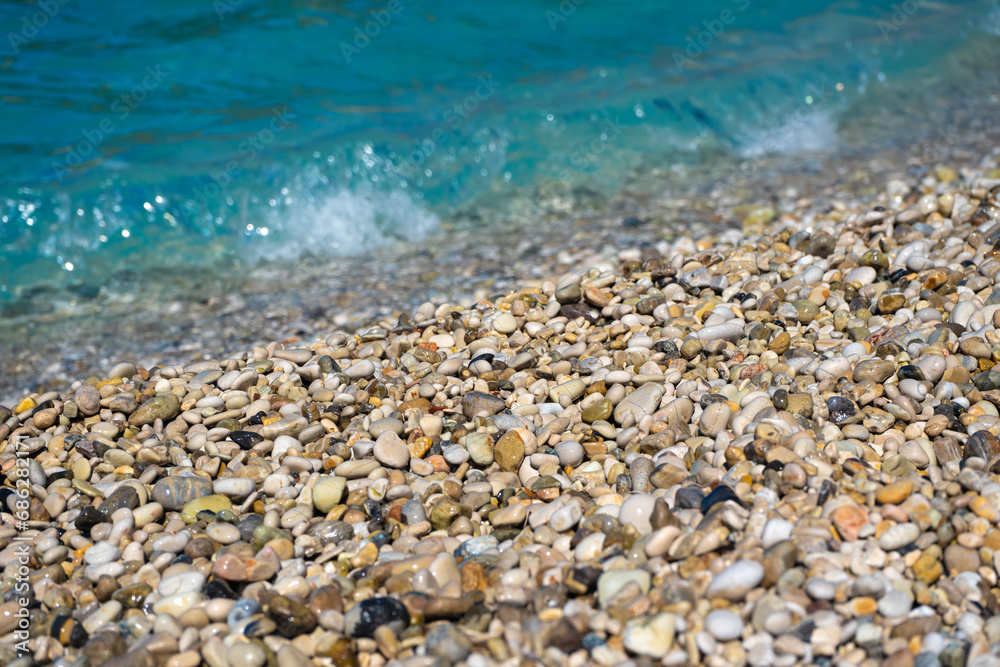 Closeup detail - small pebbles or rough sand on a beach, blurred afternoon sun lit calm sea in background Closeup detail - small pebbles or rough sand on a beach, blurred afternoon sun lit calm sea in background