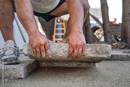 Installing new pavement or floor outside from large concrete tiles, closeup detail on male worker fitting stone block over sand and gravel base layer