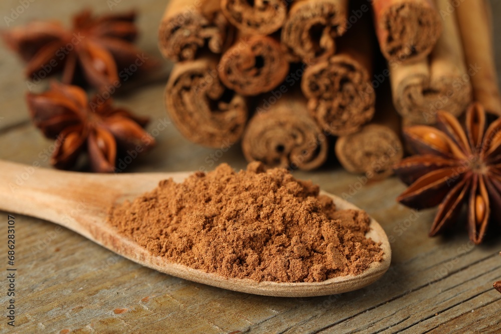 Spoon with cinnamon powder, sticks and star anise on wooden table, closeup