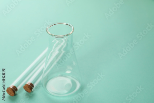 Flask and test tubes on turquoise background, space for text. Laboratory glassware