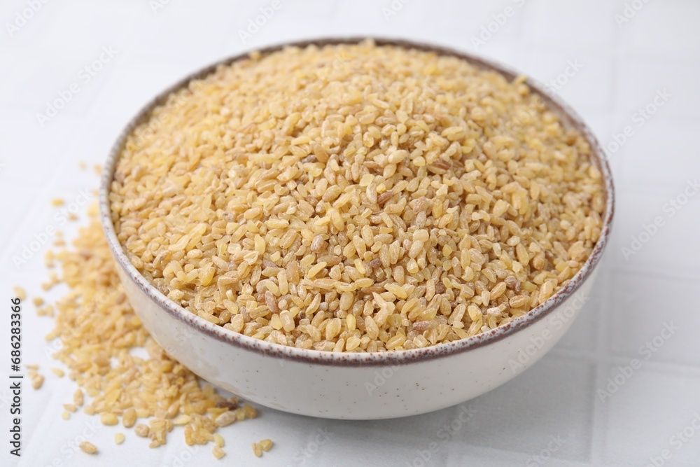 Raw bulgur in bowl on white table, closeup Raw bulgur in bowl on white table, closeup