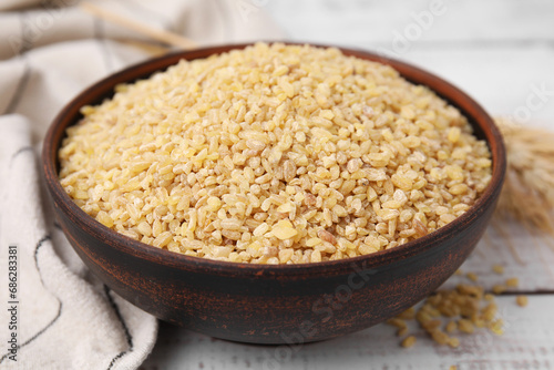 Raw bulgur in bowl on white wooden table, closeup