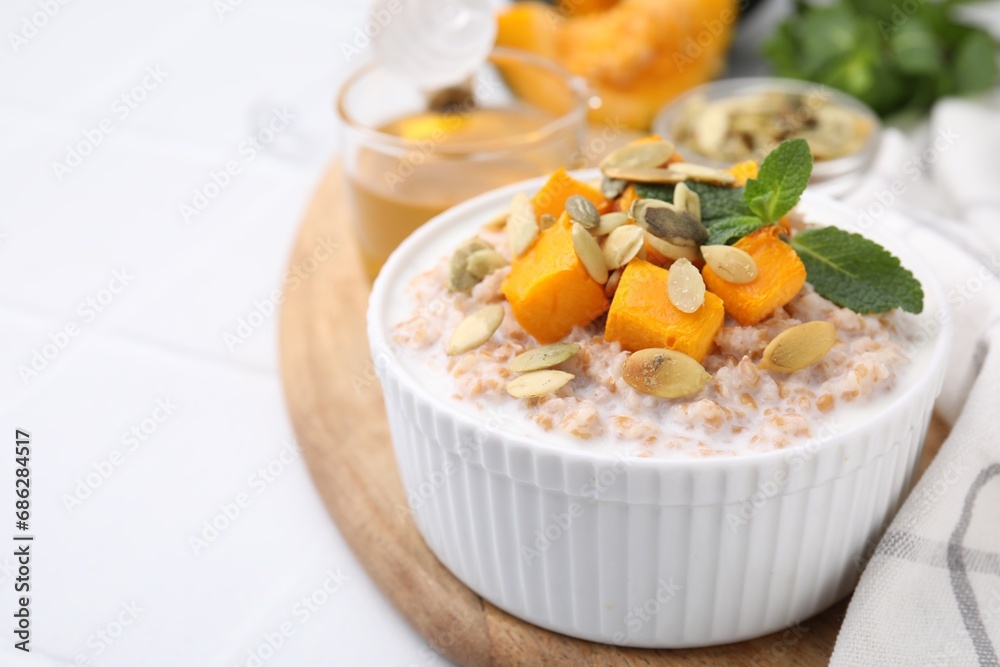 Tasty wheat porridge with pumpkin and mint in bowl on white table, closeup. Space for text Tasty wheat porridge with pumpkin and mint in bowl on white table, closeup. Space for text