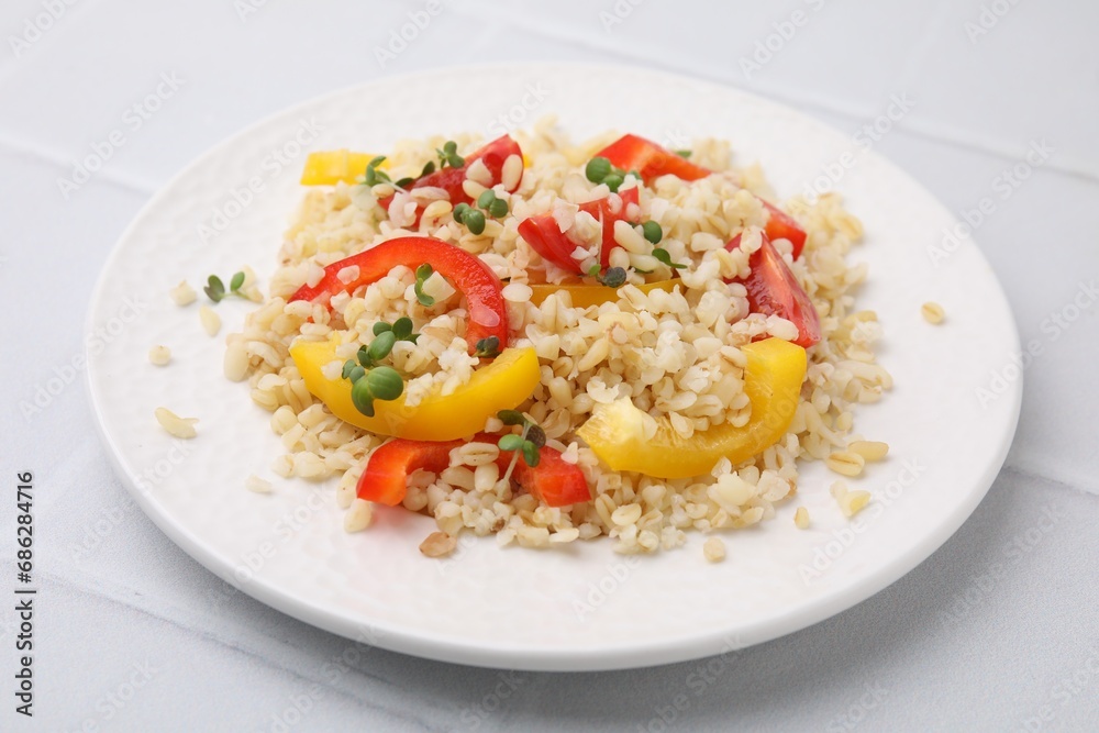 Plate of cooked bulgur with vegetables on white tiled table Plate of cooked bulgur with vegetables on white tiled table