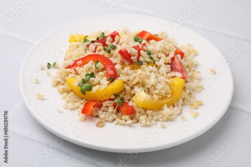 Plate of cooked bulgur with vegetables on white tiled table