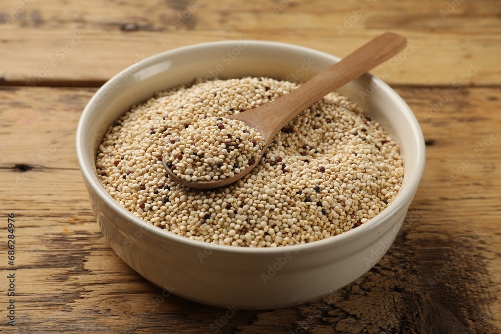 Raw quinoa seeds and spoon in bowl on wooden table, closeup Raw quinoa seeds and spoon in bowl on wooden table, closeup