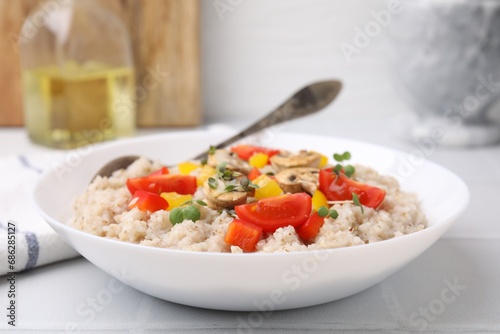 Delicious barley porridge with vegetables and microgreens in bowl on table, closeup