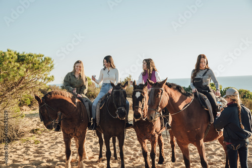 Group of female friends drinking from plastic cups while riding horses