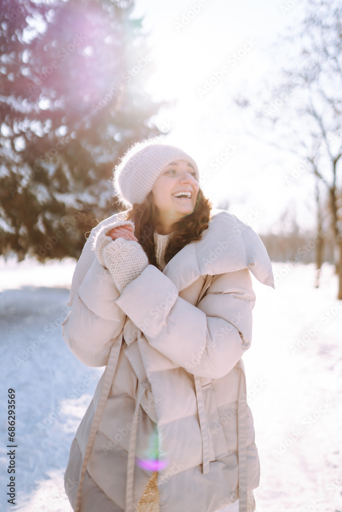 Obraz premium Winter portrait of a happy woman in a snowy park. Young woman in warm clothes having fun with snow outdoors. Fun, weekend concept