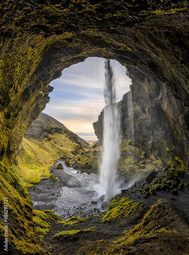 Wasserfall auf Island von hinten mit Felsbogen und grünem Moos.