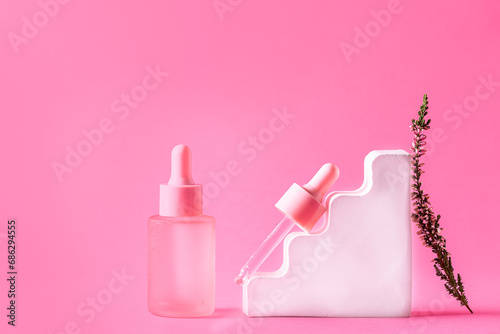 Set of skin care serums in pink bottles with dropper on bright pink background with flowers and decorations. Natural organic cosmetic products.