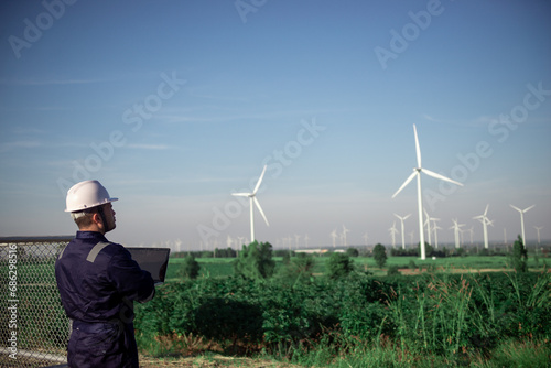 A wind turbine maintenance engineer is standing and inspecting the operation of wind turbine blades and inspecting various systems