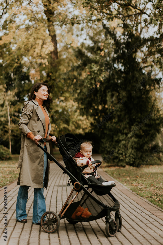 Young woman with cute baby girl in baby stroller at the autumn park
