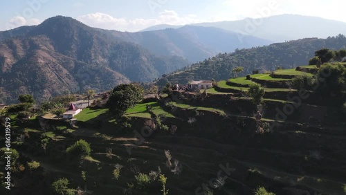 Aerial view of hilly landscape and villages in the Kumaon region of the Himalayas. Terraced houses amidst green mountains on a sunny day. Cloudy skyline in the hills of India Remote hilly areas. 4k photo