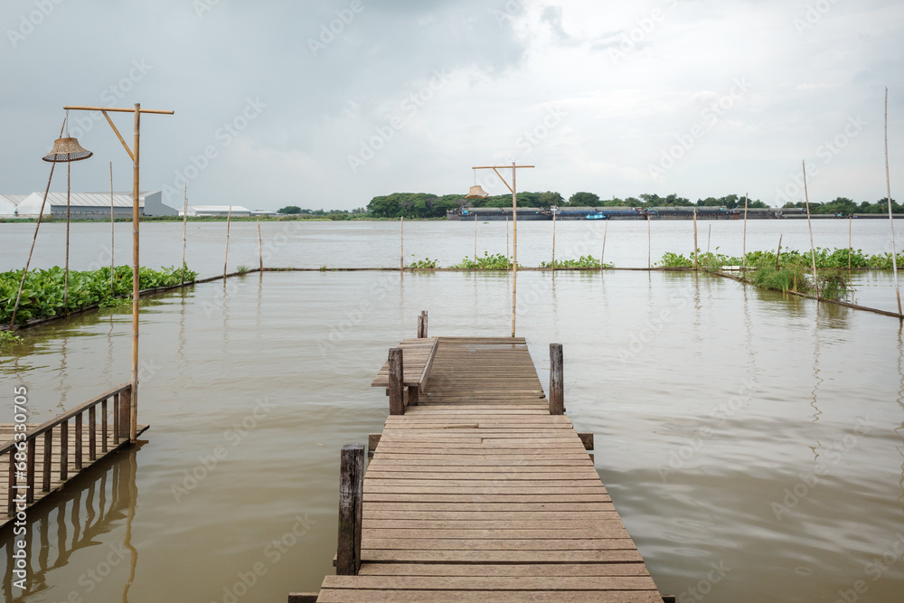 Fototapeta premium River Repose: Wooden Pier Extending into Tranquil Chao Phraya River in Thailand. 