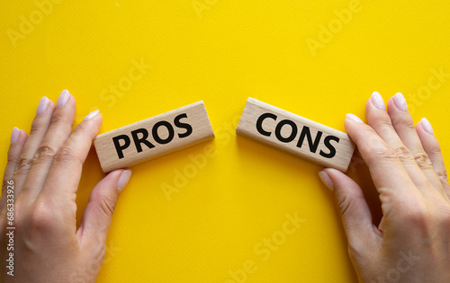 Pros vs Cons symbol. Concept word Pros vs Cons on wooden blocks. Businessman hand. Beautiful yellow background. Business and Pros vs Cons concept. Copy space