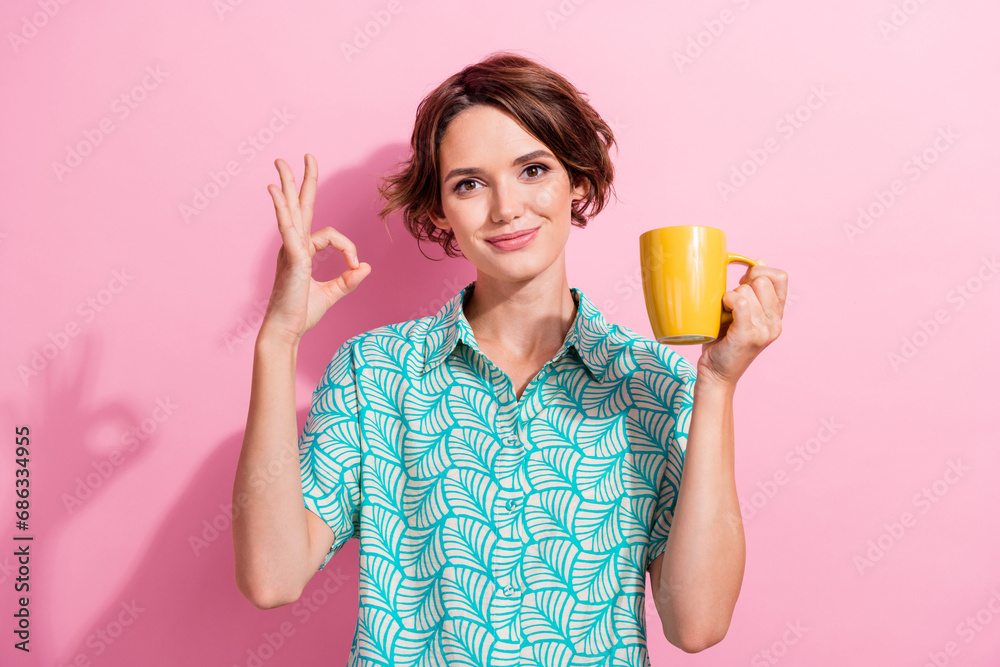 Photo of nice positive lady hold fresh coffee mug demonstrate okey symbol isolated on pink color background Photo of nice positive lady hold fresh coffee mug demonstrate okey symbol isolated on pink color background