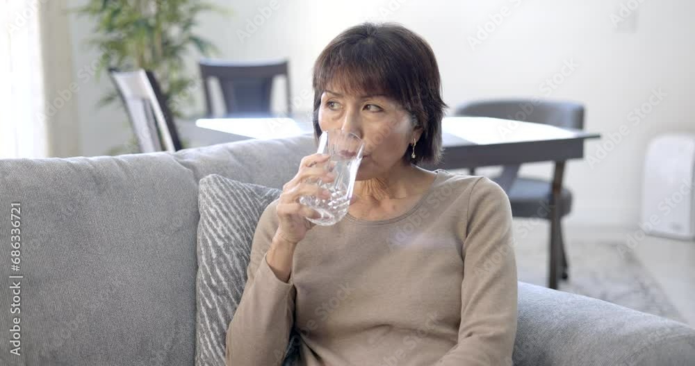 Attractive mature stylish woman peacefully drinking glass of water relaxing sitting at home