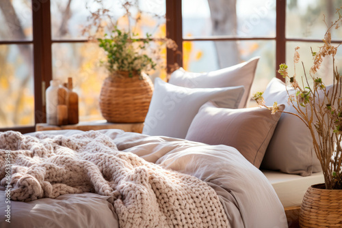Cozy bed with pillows and a blanket on the background of a large window in a rustic house