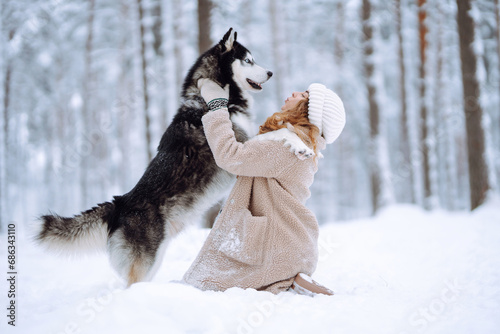 Cute woman playing with her dog in the snow. A happy woman and a Siberian husky are walking together in a snowy forest. The concept of holiday, relaxation.