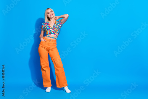 Portrait of gorgeous adorable girl wear stylish shirt orange pants hand in pocket arm on neck isolated on vivid blue color background