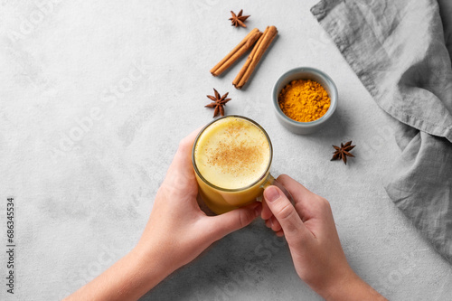 Hands holding turmeric golden milk latte with spices and honey. Detox, immunity boosting, anti-inflammatory, healthy, cozy drink