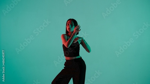 In the frame on a blue, light background. Dances young, beautiful girl. Demonstrates dance moves in the style of hip hop. Shes staring at the camera. Shes feminine in a black top and pants