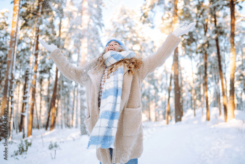 Happy woman wearing scarf and hat on snowy winter day outdoors. Young woman having fun with snow on a frosty day. Walking concept.