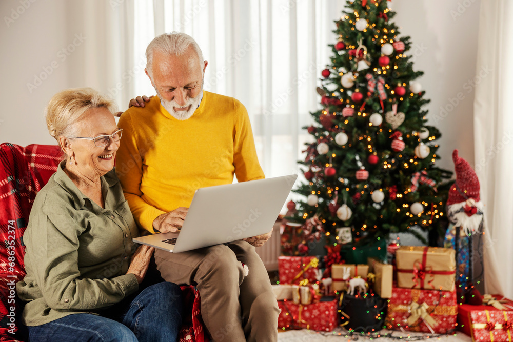A cheerful senior couple is scrolling and smiling at the laptop at home on christmas and new year. A cheerful senior couple is scrolling and smiling at the laptop at home on christmas and new year.