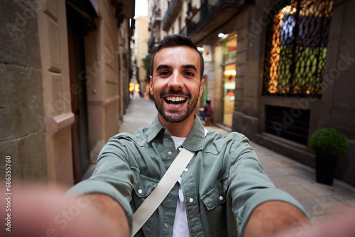 Happy selfie of a young caucasian man in an old town of Barcelona. Male tourist taking a self portrait using smartphone to post it on social media, photo