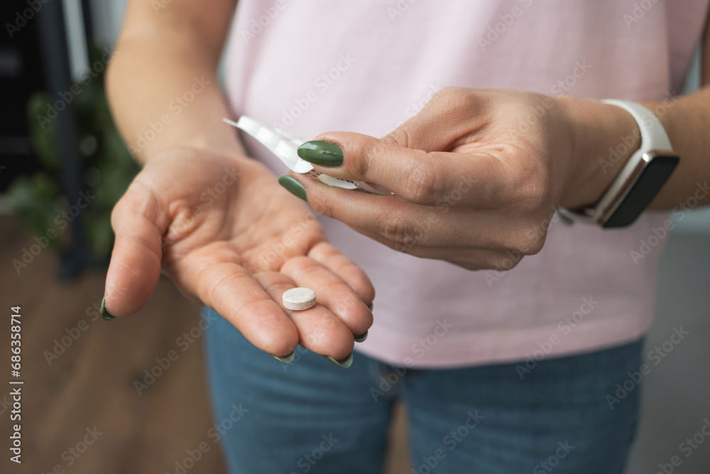 Young woman holding pill in a hand, painkiller or antibiotic, taking medicine from blister pack, close-up view Young woman holding pill in a hand, painkiller or antibiotic, taking medicine from blister pack, close-up view