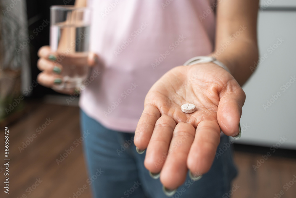 Young woman taking medicine pill, painkiller or antibiotic, holding glass of water