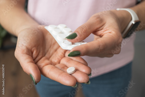 Young woman holding pill in a hand  painkiller or antibiotic  taking medicine from blister pack  close-up view