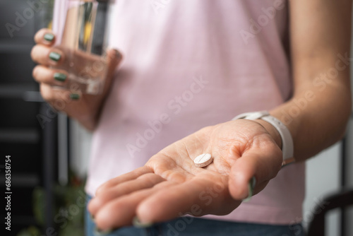 Young woman taking medicine pill, painkiller or antibiotic, holding glass of water