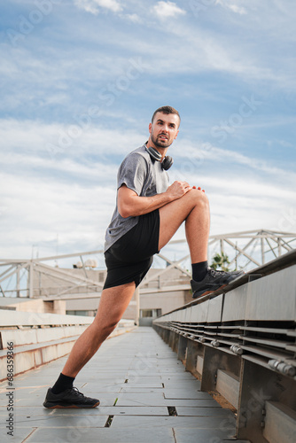 Fototapeta Naklejka Na Ścianę i Meble -  Vertical. Active sporty man stretching legs after cardio running workout. Athletic spotrsman recover his muscle in a fitness training routine having a wellness lifestyle. Guy doing a strength exercise