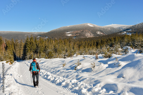 The young man is walking along the snow-covered hiking trail, from the trail you can see the mountain landscape - the Sudetes.