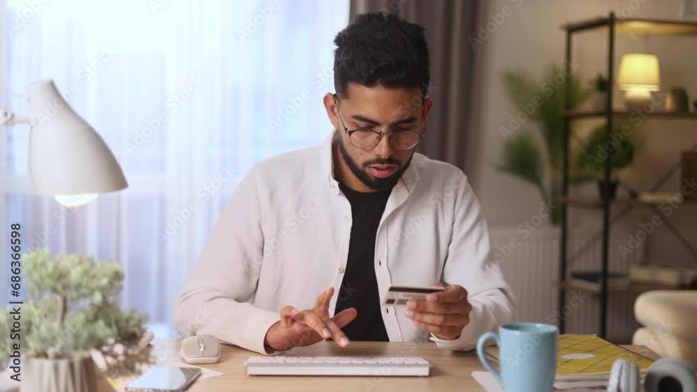 Camera view of young handsome man paying with credit card on computer at home Happy customer doing payments online shopping in internet store and receiving cashback Easy pay concept Camera view of young handsome man paying with credit card on computer at home Happy customer doing payments online shopping in internet store and receiving cashback Easy pay concept