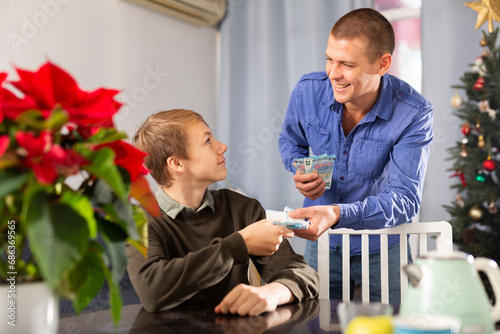 Teenager boy asking his young father for pocket money before celebrating Christmas at home