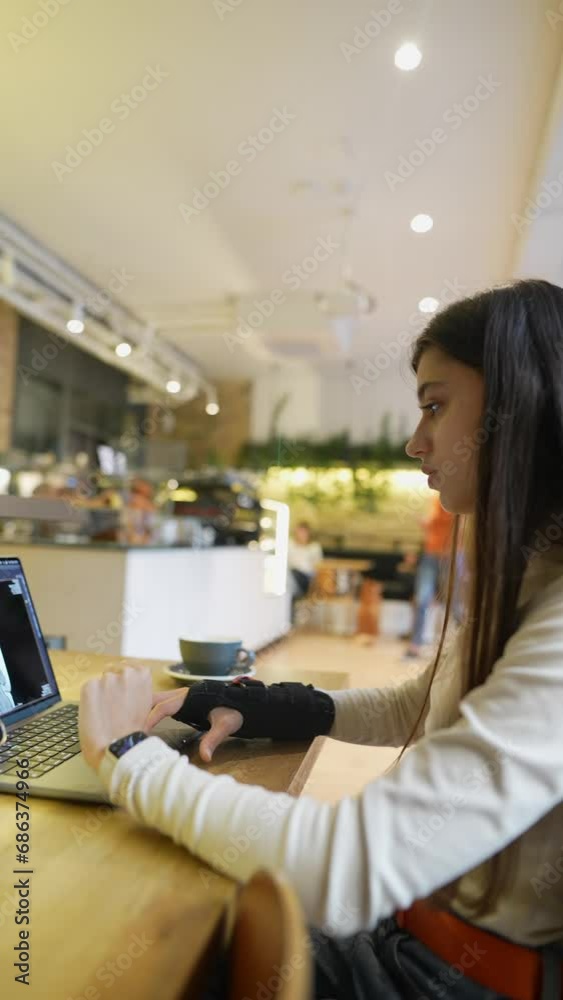 A young student studying medicine is using a laptop and a phone for online learning at a cafe. A young student studying medicine is using a laptop and a phone for online learning at a cafe.