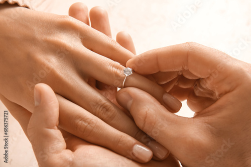 Man putting engagement ring on woman's finger against white background, closeup photo