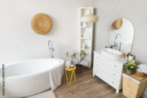 Interior of light bathroom with white sink  bathtub and shelving unit  blurred view