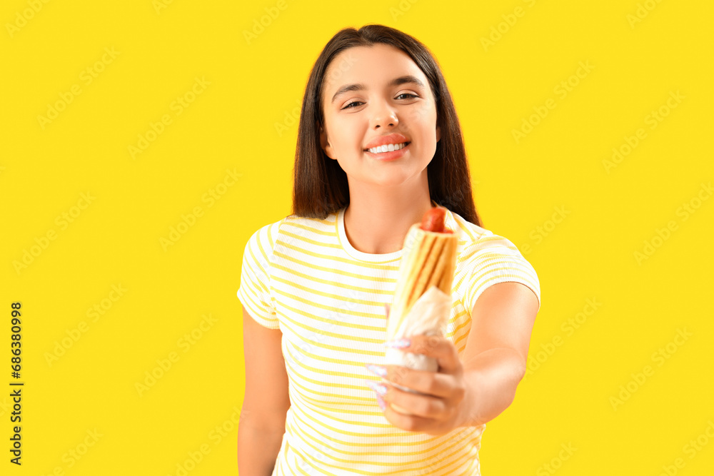 Pretty young woman with tasty french hot dog on yellow background Pretty young woman with tasty french hot dog on yellow background