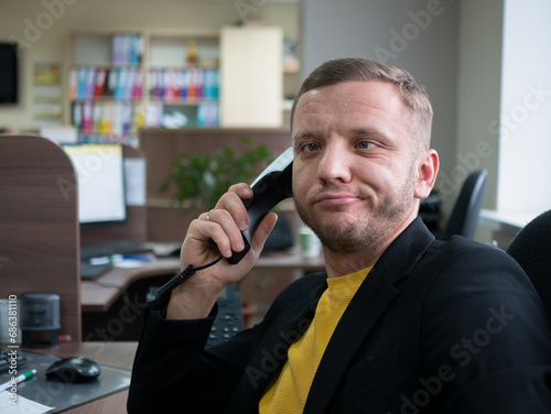 Person is working too hard, his face displays sign of exhaustion. Midlife man sitting in the office and talking on the phone