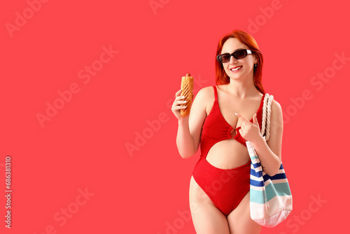 Beautiful young woman in swimsuit, with beach bag and french hot dog on red background