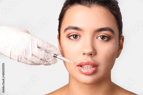 Young woman receiving lip injection on light background, closeup